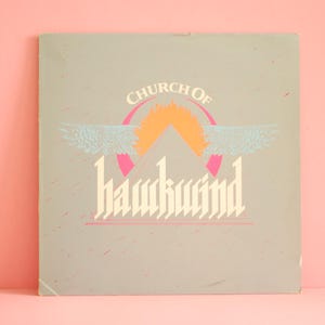 May include: A vintage album cover with the text "Church of Hawkwind" in a gothic font. The design features a pink circle, an orange sun, and light blue wings on a gray background. The album is set against a pink backdrop.