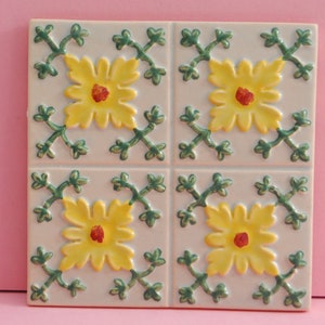 May include: Four white ceramic tiles with a floral design. Each tile features a yellow flower with a red centre surrounded by green leaves.