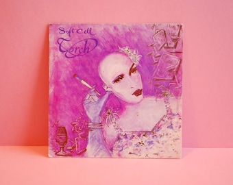Puede incluir: Una portada de álbum rosa y blanca con el texto "Soft Cell" y "Torch" en una fuente estilizada. La portada presenta una pintura de una persona con la cabeza rapada, vestida con un vestido blanco y sosteniendo un cigarrillo.