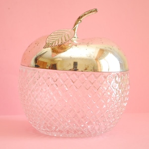 Könnte beinhalten: Eine klare, apfelförmige Schale aus Glas mit einem silbernen Deckel und einem goldenen Blattdesign. Die Schale hat ein Diamantenmuster.