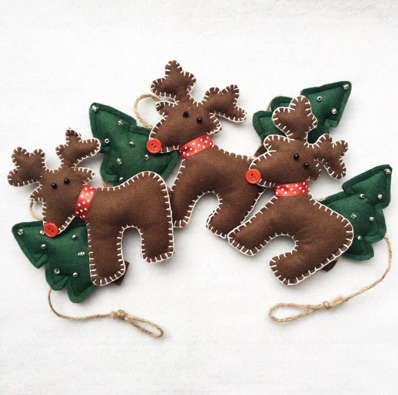 May include: A garland of three brown felt reindeer with red and white polka dot bows and green felt Christmas trees. Each reindeer has a red button nose and black eyes.