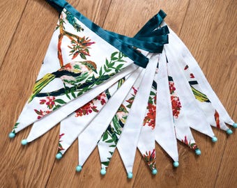 May include: A decorative bunting featuring white triangular flags with a bird and floral pattern. The bunting has teal trim, teal bead details, and is ideal for celebrations. Each flag is approximately 15 cm long.