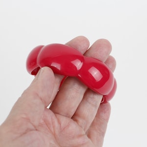 May include: A red plastic bangle bracelet with a rounded, bulbous design.
