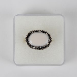 May include: A white oval ring with a silver rope-like design around the stone.