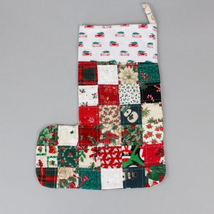 May include: A patchwork Christmas stocking with a red, green, and white color scheme. The stocking is made of various fabrics with different Christmas-themed patterns, including plaid, holly, and candy canes.