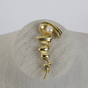 May include: A gold-toned brooch with a swirling design and a single white pearl accent.