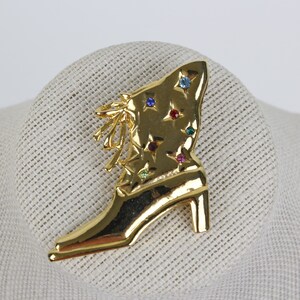 May include: A gold-tone boot brooch with a star design and colorful rhinestones.