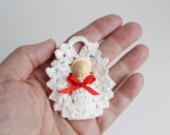 May include: A small white crocheted angel ornament with a red ribbon bow. The angel is holding a small white doll with a halo.