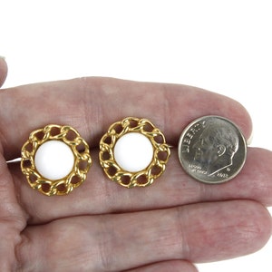 May include: A pair of gold tone earrings with white round cabochon stones set in a chain link design. The earrings are shown next to a US dime for size comparison.