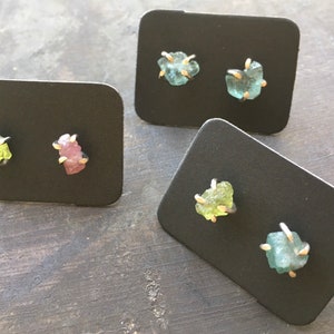 Pu&ograve; includere: Quattro paia di orecchini con pietre preziose grezze incastonate in argento. Le pietre preziose sono verdi, rosa e blu.