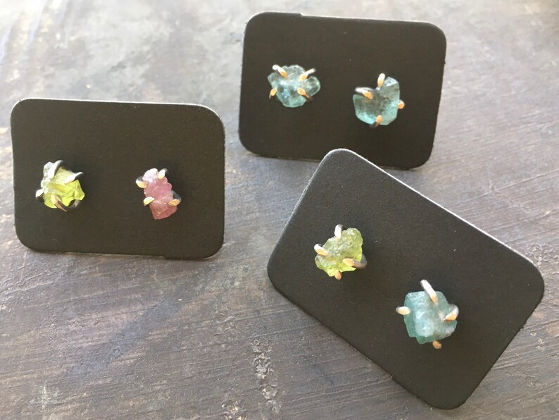 Pu&ograve; includere: Quattro paia di orecchini con pietre preziose grezze incastonate in argento. Le pietre preziose sono verdi, rosa e blu.