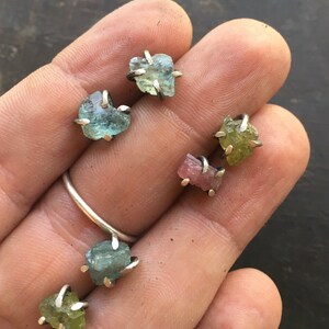 Pu&ograve; includere: Sei piccoli orecchini con pietre preziose grezze con montature in argento. Le pietre preziose sono acquamarina, turmalina rosa e peridoto verde.