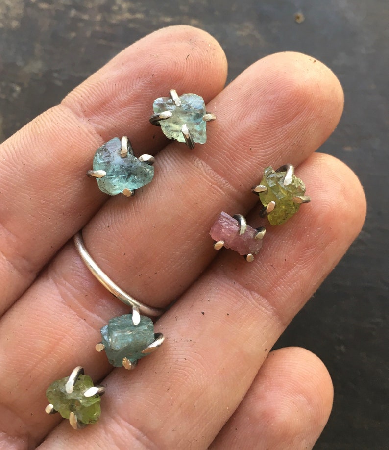 Pu&ograve; includere: Sei piccoli orecchini con pietre preziose grezze con montature in argento. Le pietre preziose sono acquamarina, turmalina rosa e peridoto verde.