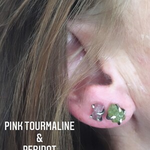 Pu&ograve; includere: Primo piano di un orecchio che indossa un paio di orecchini. L'orecchino sinistro presenta una pietra preziosa di tormalina rosa, mentre l'orecchino destro presenta una pietra preziosa di peridoto verde. Entrambi gli orecchini sono incastonati in argento.