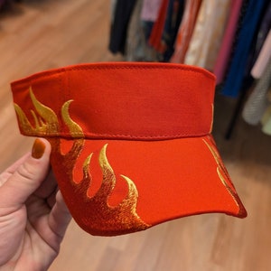 Puede incluir: Visera roja con un dise&ntilde;o de llama bordado en oro.