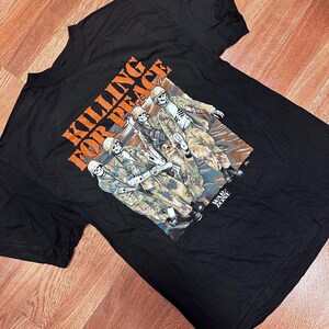 May include: Black t-shirt with a graphic print of skeletons dressed as soldiers. The text "KILLING FOR PEACE" is printed in orange above the graphic. The text "WAR ZONE" is printed in white below the graphic.