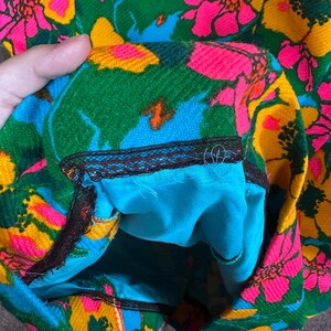 May include: A garment featuring a vibrant floral pattern in shades of hot pink, yellow, and green on a blue background. The interior is lined with solid turquoise fabric and finished with a dark brown lace trim along the inner seam edge.