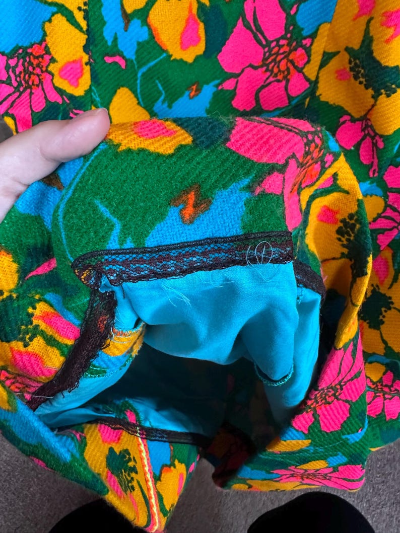 May include: A garment featuring a vibrant floral pattern in shades of hot pink, yellow, and green on a blue background. The interior is lined with solid turquoise fabric and finished with a dark brown lace trim along the inner seam edge.