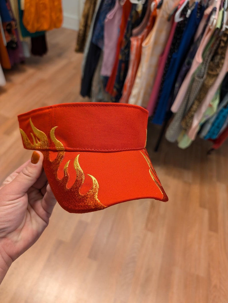 Puede incluir: Visera roja con un dise&ntilde;o de llama bordado en oro.