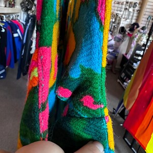 May include: A thick, felted fabric bag featuring a vibrant, abstract pattern in bright shades of hot pink, electric blue, forest green, and golden yellow. The material has a fuzzy, textured surface with visible stitched seams along the edges.