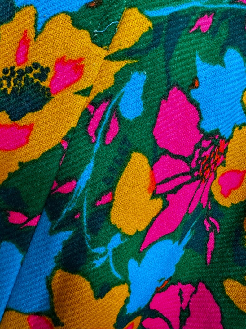 May include: A textile fabric featuring a vibrant floral pattern with bold, saturated colours. The design includes large, stylised flowers in shades of hot pink, mustard yellow, and bright sky blue, set against a deep forest green background.