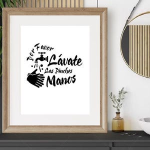 May include: A framed print with the text "Por Favor Lávate Las Pinches Manos" in black. The artwork features a faucet, water droplets, and a pair of hands. The frame is a light brown color.
