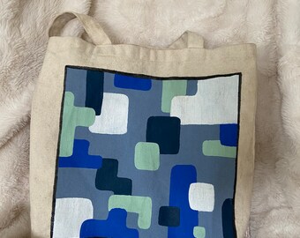 Puede incluir: Una bolsa de lona beige con un estampado geométrico azul, verde y blanco impreso en la parte delantera.