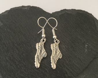 May include: A pair of silver earrings featuring a detailed shoe design. The earrings are on a black background.