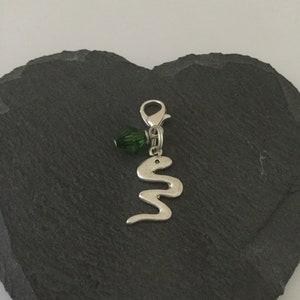 May include: Silver charm featuring a snake design and a green crystal bead. The charm has a lobster clasp.