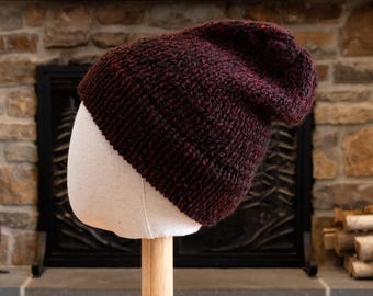 May include: A dark red and black knit beanie hat on a white mannequin head. The hat is slouchy and has a textured knit.