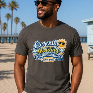 May include: Dark gray t-shirt with the text "Currently Avoiding Responsibilities since 9am" in a blue, yellow, and white design. The graphic includes a smiling sun wearing sunglasses. The shirt is worn on a beach.