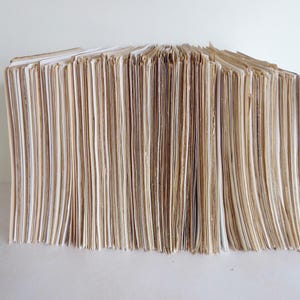 May include: A stack of brown and white paper, likely pages from a book or journal, are stacked neatly on a white surface.
