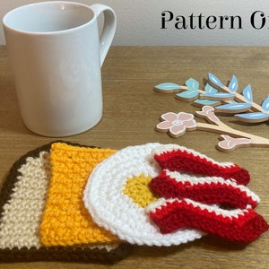 May include: Crocheted breakfast food coasters, including a brown toast, yellow scrambled eggs, white fried egg, and red bacon. The coasters are on a wooden surface next to a white mug.