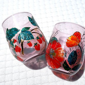Puede incluir: Dos vasos de vidrio transparente con diseños florales pintados. Un vaso presenta bayas rojas y hojas verdes, mientras que el otro presenta amapolas rojas y naranjas con hojas verdes.