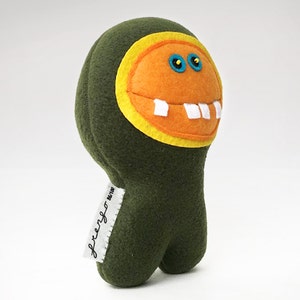 May include: Green plush toy with a large orange smiling face, yellow eyes, and white teeth. The toy has a tag that says "freengo" on it.