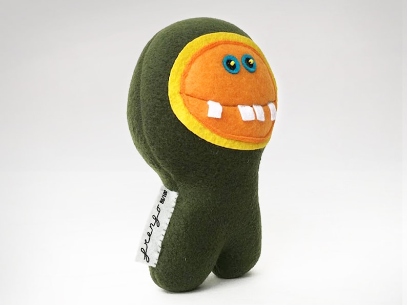 May include: Green plush toy with a large orange smiling face, yellow eyes, and white teeth. The toy has a tag that says "freengo" on it.
