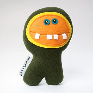 May include: A green plush toy with a large orange face, yellow eyes, and white teeth. The toy has a tag that says "freaky" on it.