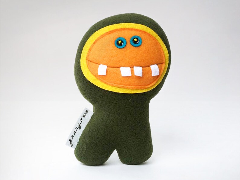 May include: A green plush toy with a large orange face, yellow eyes, and white teeth. The toy has a tag that says "freaky" on it.