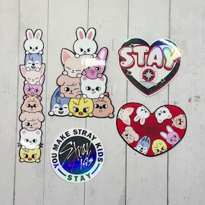 May include: A selection of stickers with cartoon animal characters and the text "STAY" and "YOU MAKE STRAY KIDS STAY". The stickers are in various shapes, including a heart and a circle, with holographic and colourful designs.