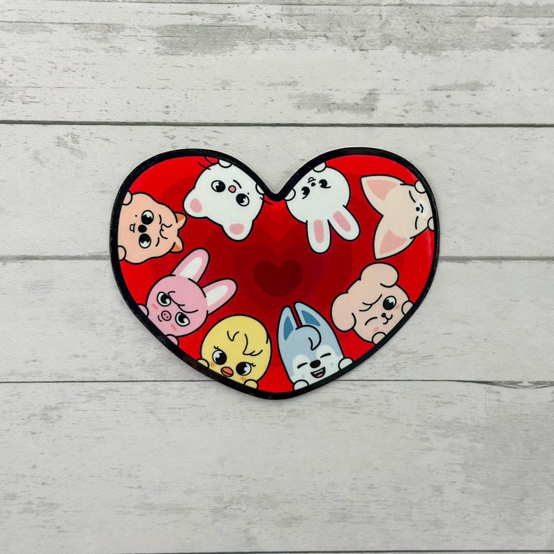 May include: A heart-shaped sticker with a red background and a black border. The sticker features cartoon animal faces in various colours, including white, pink, yellow, and blue. The animals are arranged around the heart's centre.