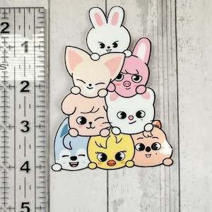 May include: A sticker depicting a pile of cartoon animals: a rabbit, fox, pig, dog, chick, and bear. The sticker has a white outline and is set against a light wood grain background. The characters have cute expressions.