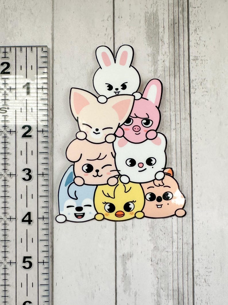 May include: A sticker depicting a pile of cartoon animals: a rabbit, fox, pig, dog, chick, and bear. The sticker has a white outline and is set against a light wood grain background. The characters have cute expressions.