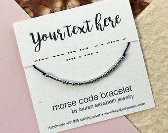 May include: A black cord bracelet with silver-colored beads arranged in a Morse code pattern, displayed on a white card featuring the text Your text here, morse code bracelet, by lauren elizabeth jewelry, and handmade with 925 sterling silver.
