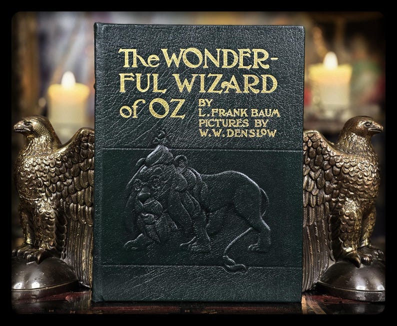 Puede incluir: Un ejemplar antiguo de "The Wonderful Wizard of Oz" de L. Frank Baum, con letras doradas y una cubierta verde oscuro con una ilustraci&oacute;n de un le&oacute;n. A ambos lados del libro, dos sujetalibros de &aacute;guila de bronce crean una exhibici&oacute;n literaria cl&aacute;sica.