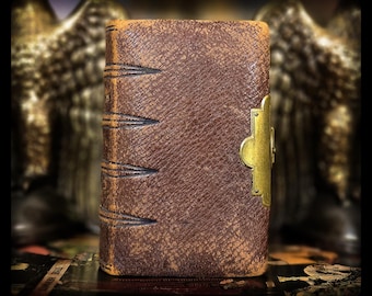 May include: A close-up of a vintage, brown leather-bound book with a gold-colored clasp. The book's spine features decorative stitching. The leather has a textured appearance, suggesting age and use. The background is blurred, with hints of gold and dark tones.