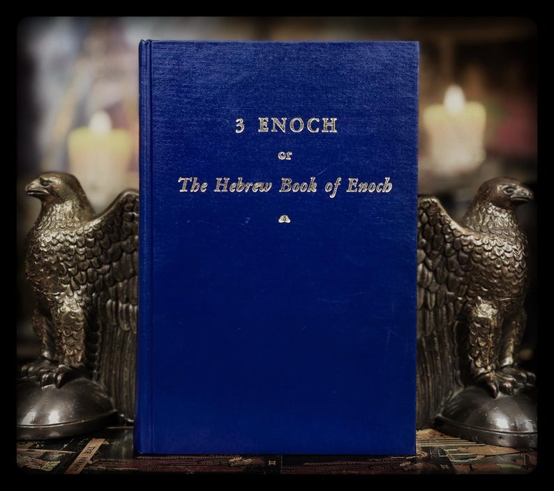 May include: A blue hardcover book with the title "3 Enoch or The Hebrew Book of Enoch" in silver lettering. Two bronze eagle bookends frame the book, with candles softly lit in the background.
