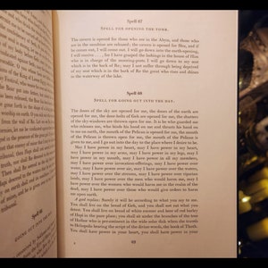 以下が含まれることがあります： 黄ばんだページを開いた本のクローズアップ。ページのテキストには、「Spell 67 SPELL FOR OPENING THE TOMB.」と「Spell 68 SPELL FOR GOING OUT INTO THE DAY.」と書かれている。