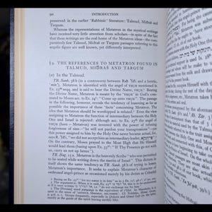 May include: An open book discussing Metatron, a figure in Jewish mysticism. The pages are aged, with English text. A lit candle in the background provides a warm light.