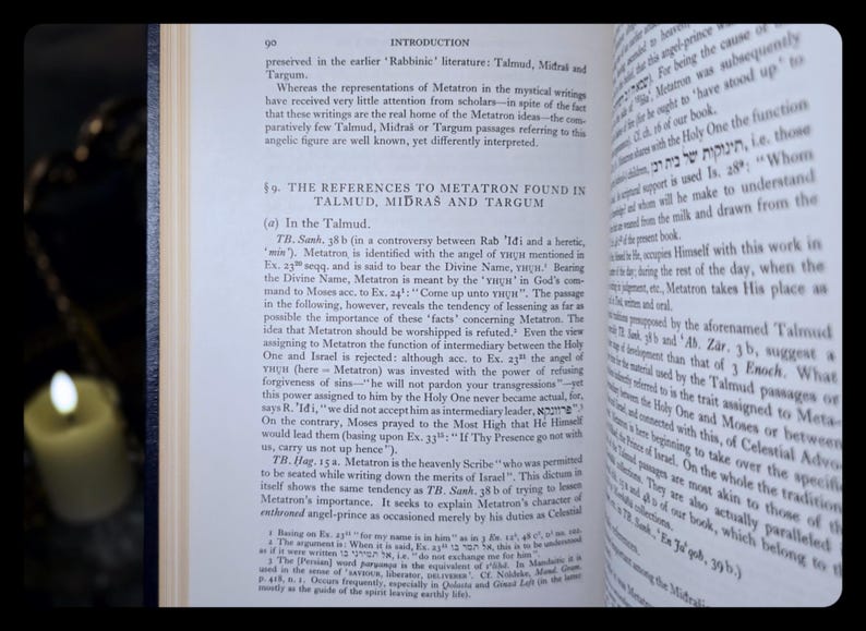 May include: An open book discussing Metatron, a figure in Jewish mysticism. The pages are aged, with English text. A lit candle in the background provides a warm light.