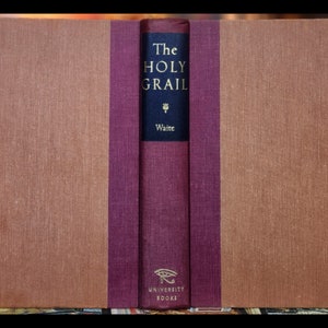 May include: A burgundy and brown hardcover book with the title "The Holy Grail" by Arthur Edward Waite. The book is part of the University Books series.
